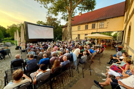 Viele Menschen sitzen draußen und schauen auf eine große Kinoleinwand