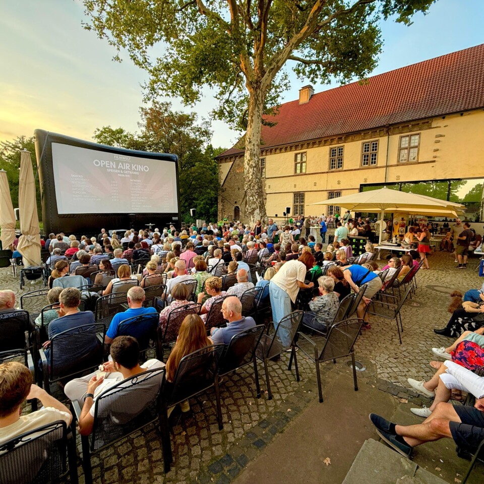 Viele Menschen sitzen draußen und schauen auf eine große Kinoleinwand