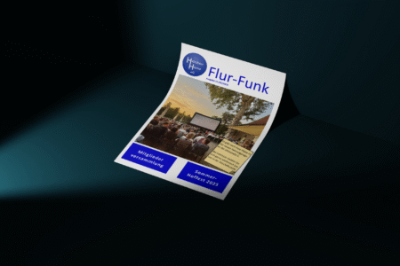Eine Ausgabe des „Flur-Funk“-Mitgliedermagazins der Heimbau Herne eG liegt auf einer dunklen Oberfläche. Auf dem Cover sind ein Open-Air-Event und Informationen zur Ausgabe zu sehen.
