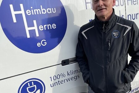 Ein Mann in dunkler Arbeitsjacke steht vor einem Firmenfahrzeug mit dem Logo der Heimbau Herne eG.