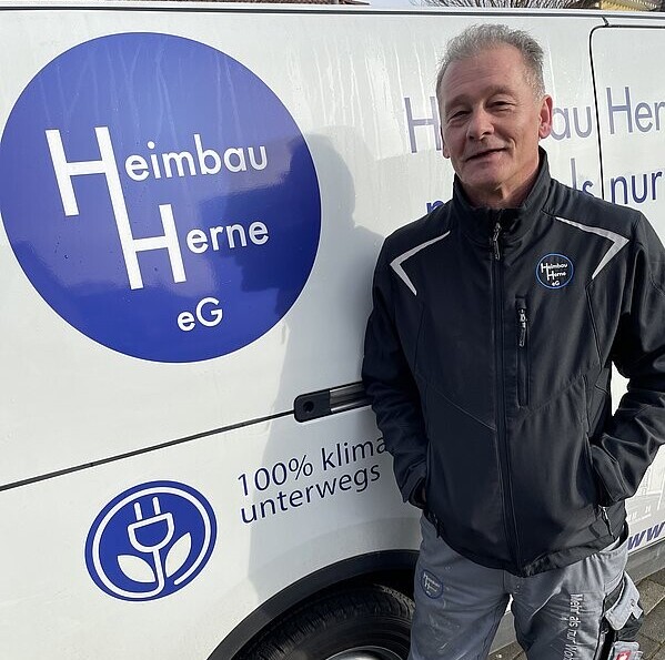 Ein Mann in dunkler Arbeitsjacke steht vor einem Firmenfahrzeug mit dem Logo der Heimbau Herne eG.
