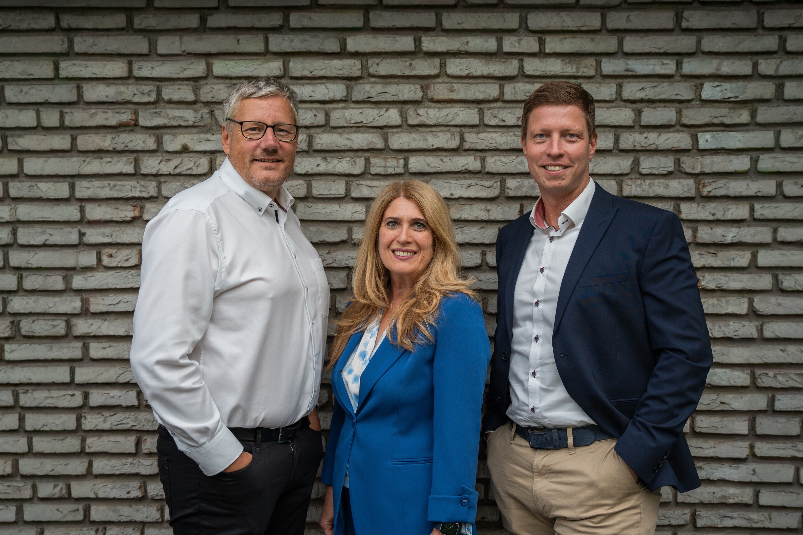 Dei Personen stehen schick gekleidet vor einer Steinwand