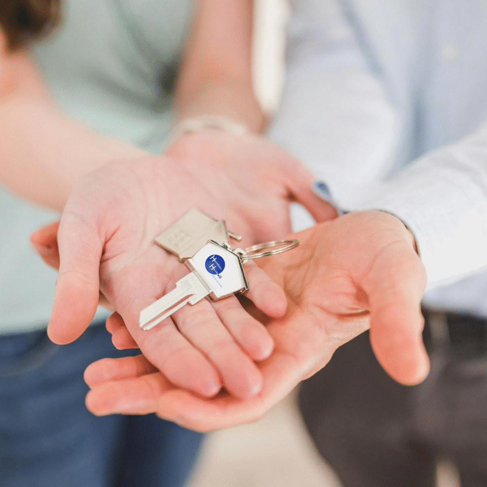 Zwei Personen strecken ihre Hände Richtung Kamera aus und halten in der Handfäche einen Wohnungsschlüssel mit dem Heimbau Logo drauf