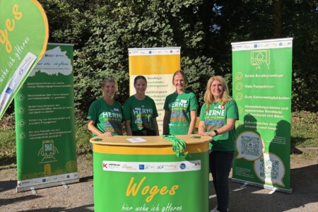 vier Frauen stehen auf einer Berufsmesse an ihrem Stand. Der Stand und die Klamotten der Personen sind grün