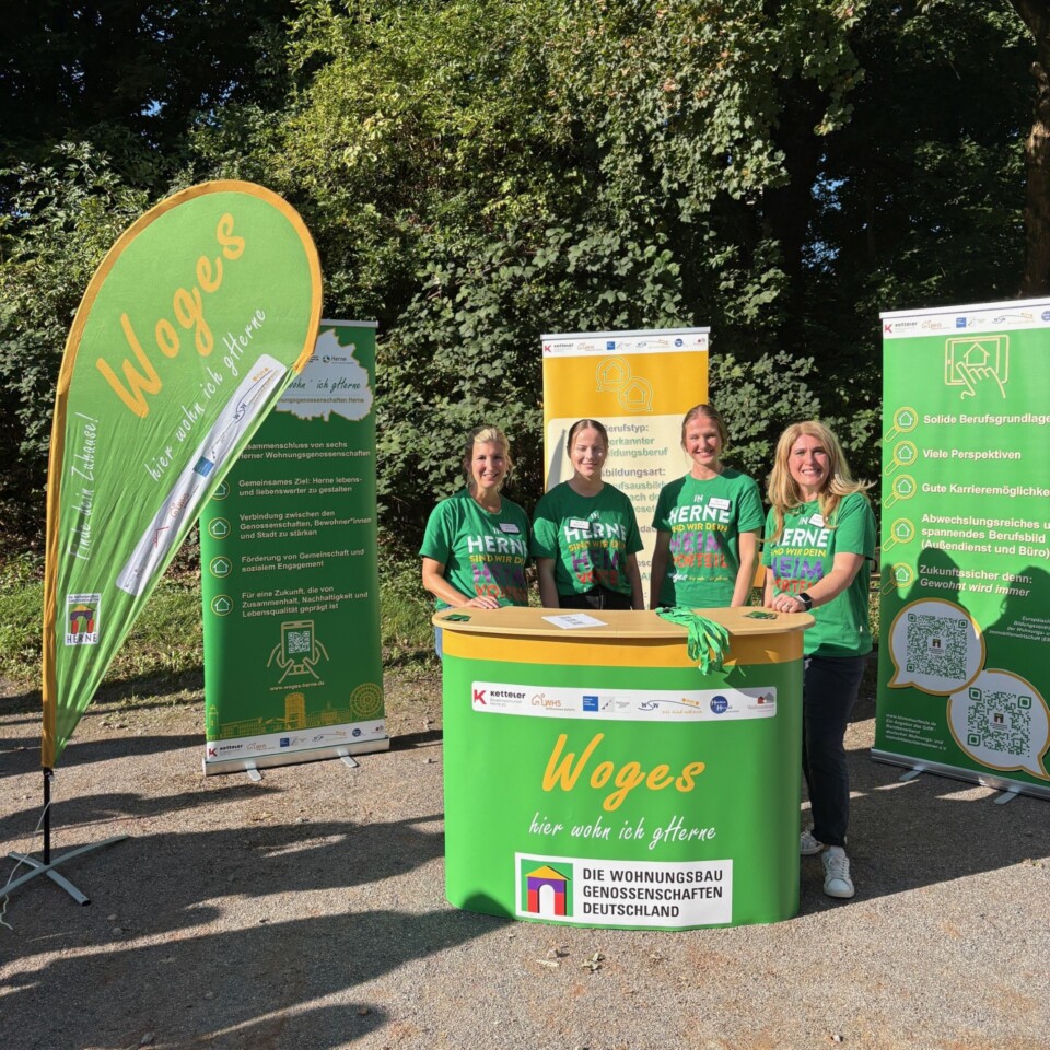 vier Frauen stehen auf einer Berufsmesse an ihrem Stand. Der Stand und die Klamotten der Personen sind grün