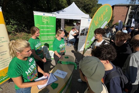 Menschen stehen auf einer Berufsmesse an einem Stand. Der Stand und die Klamotten der Personen sind grün