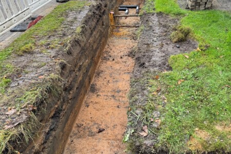 Ein langes ausgehobenes Loch im Boden. Links und rechts stehen Bauzäune
