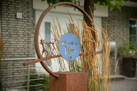 Es ist eine Kupferskulptur vor der Geschäftsstelle abgebildet. In der Mitte der Skulptur befindet sich das Firmenlogo der Heimbau Herne eG