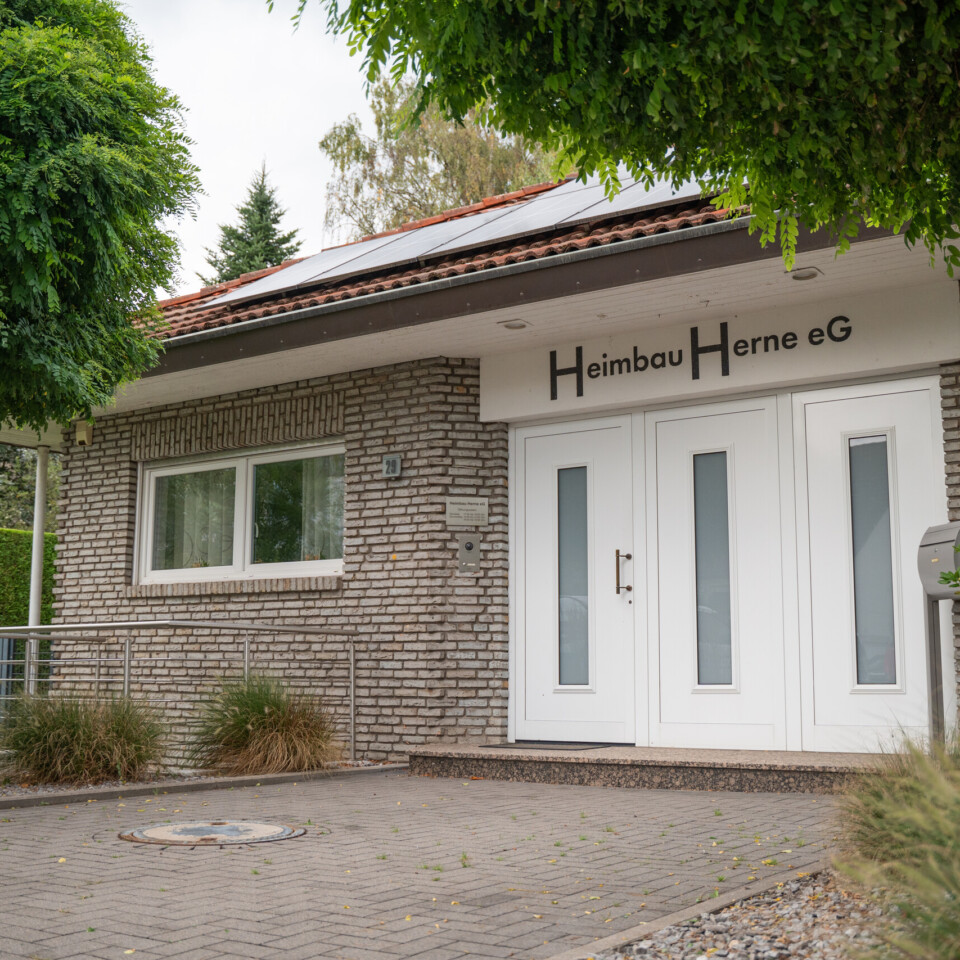 Außenaufnahme eines einstöckigen Hauses mit weißer Eingangstür, gemauerten Fassadesteinen und gepflegter Bepflanzung im Vordergrund.