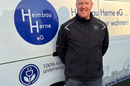 Ein Mann in dunkler Arbeitsjacke steht vor einem Firmenfahrzeug mit dem Logo der Heimbau Herne eG.