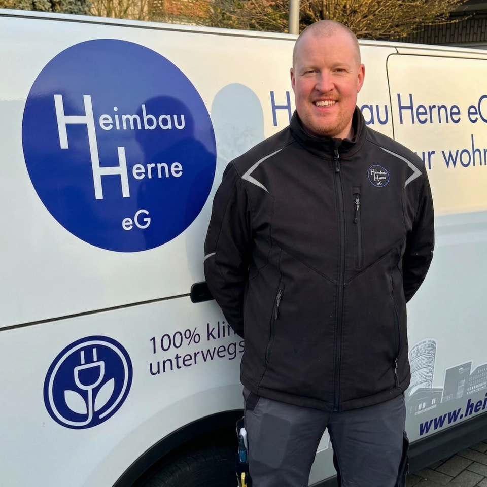 Ein Mann in dunkler Arbeitsjacke steht vor einem Firmenfahrzeug mit dem Logo der Heimbau Herne eG.